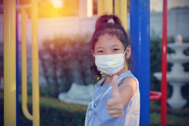 Tıbbi maske takan Asyalı kız Coronavirus 'u koruyor, tek başına oturuyor, bahçedeki kameraya bakıyor ve 