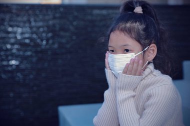 Yeni normal kavramları ve sosyal mesafeleri kabul et. Tıbbi maske takan Asyalı kız Coronavirus 'u koruyor, üzgün bir ifadeyle tek başına oturuyor. Herkes her evden çıkışında maske takmalı..