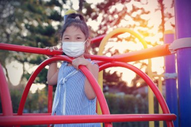 Tıbbi maske takan Asyalı kız bahçedeki kameraya bakarak koronavirüsü koruyor. Konsept evde kalmak, sosyal uzaklık, Yeni normal