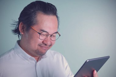 Beyaz gömlek ve gözlük takan Asyalı işadamı yeşil arka planda gülümseyen tablete bakıyor. Konsept iş, teknoloji, İnternet sonraki çalışma.