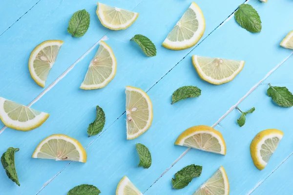 Concept background, flat lay, top view. Lemon cut slices with mint leaf pattern on blue wooden background.