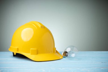 Fikir tasarımı kavramı ve iş güvenliği. Kişisel koruyucu ekipman. Mavi ahşap masa üzerinde ampul ve fotokopi alanı olan sarı başlık..