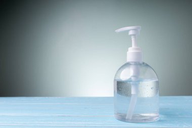 Mavi masada üzerinde fotokopi alanı olan şişe alkolü yeşil arka planda. Herkes ellerini sık sık yıkamalı, tıbbi maske takmalı..