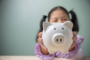 Asyalı güzel küçük şirin kız elinde kopya alanı olan beyaz domuz kumbarası tutuyor. Geleceğe eğitim için para biriktiriyor. Finansal, çocukluk, tasarruf, eğitim planlama kavramı.