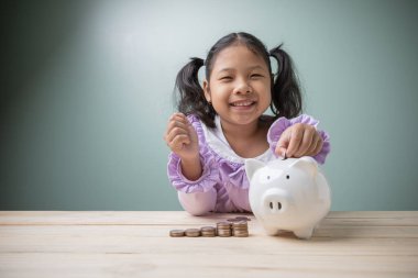 Asyalı şirin bir çocuğun gülümsemesi mutluluk, kumbarayı eski ahşap bir masanın üzerine siyah bir hesap makinesiyle bırakmak için para saymaktır. Eğitim geleceği için para biriktirme kavramı.