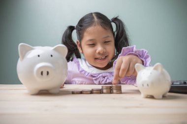 Yakışıklı bir Asyalı çocuk kumbarayı eski ahşap bir masaya siyah bir hesap makinesiyle bırakmak için para sayıyor. Eğitim geleceği için para biriktirme kavramı.