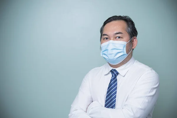 Asian businessman wearing white shirt with blue tie and wearing a medical nose mask, standing with arms crossed. Looking at the camera with copy space. Business, Social distances, new normal concept.