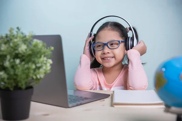 Concept learning online social distance. Asian kids girls wearing glasses, headphones smile happily looking at a laptop. Listen to online lessons from teachers. learning from home in the room personal