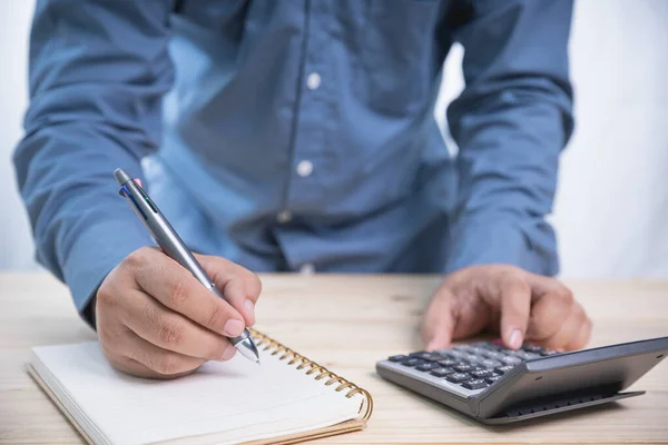 İnternet, iş ve ağ konsepti. Not defteri için elinde kalem tutan yetişkin bir işadamı. Hesap makinesi kullan. Fotokopi alanı olan bir ofisin ahşap masasında kar işi hesapla..