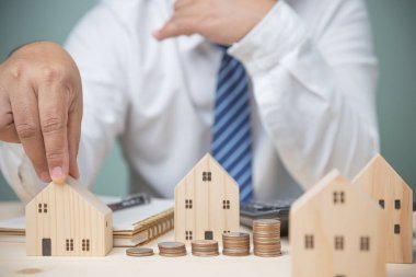 Kullanmayı düşünen bir işadamı ahşap masa üzerinde bozuk paralar olan küçük ahşap ev modelini seçer. Geleceğe yatırım yapmak için yatırım yapmak. Kredi, tasarruf, finansal konsept.