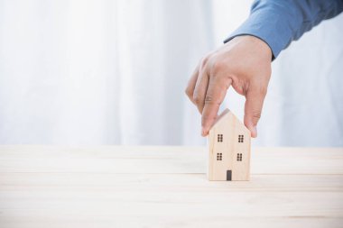 Eski ahşap bir masada mini ahşap ev modeli tutan bir iş adamı. Yatırım şirketinden gelecek kar için gelir elde ediyoruz. Sigorta, kredi, finans ve bankacılık yatırım kavramı.