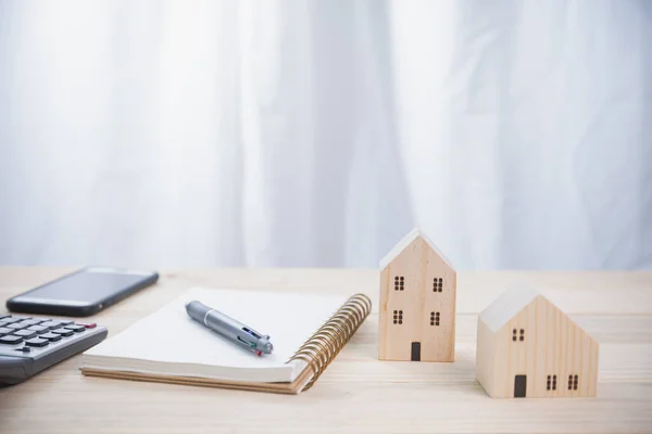 Küçük ahşap evler, modeller, defter, hesap makinesi ve ahşap masada akıllı telefon olan bir arka plan ofisi. Konsept yatırım için para hesaplar gayrimenkul, kredi, tasarruf ve bankacılık.
