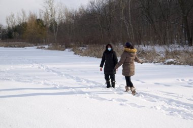 Toronto, Ontario / Kanada - 02-14-2021: Kadınlar kışın donmuş gölde maskeyle yürüyorlar. Covid-19, kış, dışarıda, sağlıklı bir yaşam tarzı..