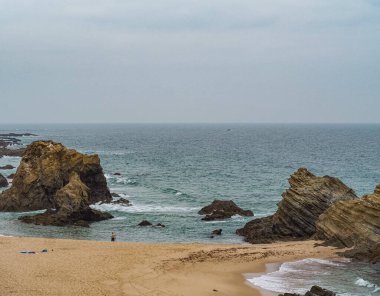 Kasvetli havada, Costa Vicentina 'da, Alentejo' da, Portekiz 'de, bomboş sahilde yapayalnız bir insan.