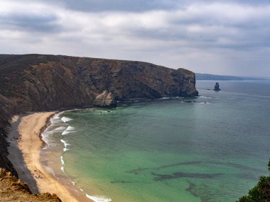 Costa Vicentina, Alentejo, Portekiz 'deki mavi ve yeşil suları ve uçurumları olan cennet boş bir plaj.