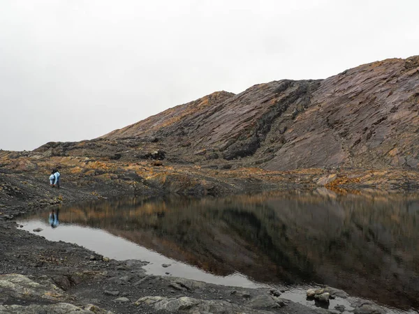 Moody landscape of mountains and lagoon with person looking at reflection in Nevado Pastoruri, Huaraz, Peru