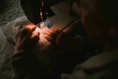 Kafkasyalı büyükannenin diktiği lambayla dikiş makinesinin kumaşını kapat.