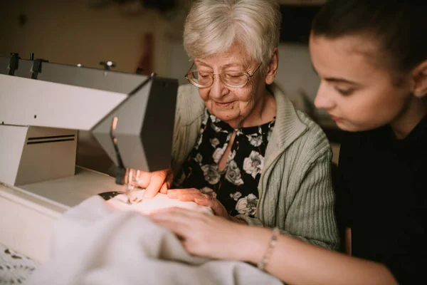 미소짓는 할머니와 손녀가 재봉틀에 가르쳐 주면서 이야기 — 스톡 사진