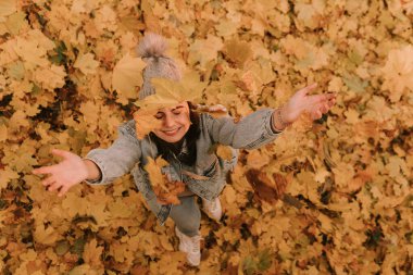Havaya yapraklar fırlatırken kot giymiş, gülümseyen beyaz bir genç kızın en iyi görüntüsü. Parkta sarı sonbahar