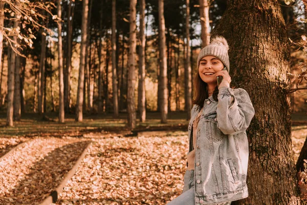 청바지를 모자를 소녀가 휴대폰에서 연설을 카메라를 봅니다 공원에서 걷는다 — 스톡 사진
