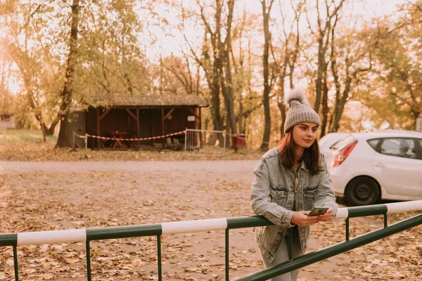 공원의 울타리에 기대어 청바지를 모자를 현대의 인디오 소녀는 전화를 — 스톡 사진