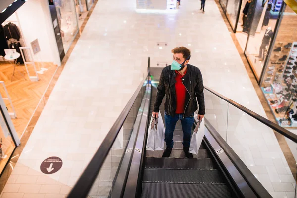 Egy Jóképű Férfi Táskákkal Kezében Arcmaszkkal Mozgólépcsőn Egy Bevásárlóközpontban Ruhavásárlás — Stock Fotó