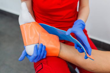 Doktorun muayenehanesinde ayak bandajı yapan kadın doktoru yakından çek. İlk yardım