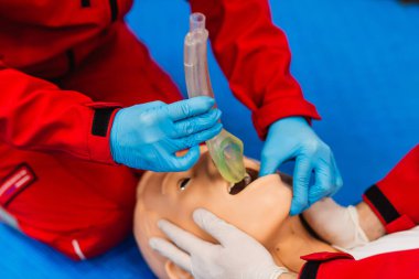 Tıbbi manken kullanarak endotrakeal entübasyon eğitimi alan kırmızı üniformalı iki sağlık görevlisinin yan görüntüsü. Yakın çekim.