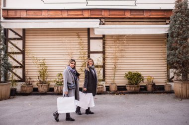 Parkta iki güzel genç kadın ellerinde çantalarla poz veriyorlar. Sonbahar alışverişi