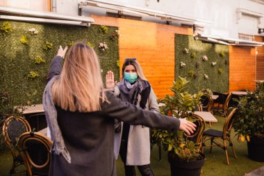 Koruyucu yüz maskesi takan iki güzel genç kadın selamlaşır.