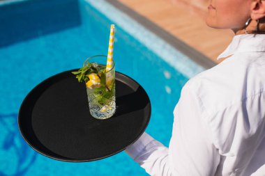 A waitress in a white shirt serves a mojito cocktail to guests by the pool. Outdoor summer party clipart