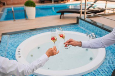 Yaz tatilleri konsept imajı. Güneşli bir yaz öğleden sonrasında, havuz kenarında bir terasta iki bardak soğuk şampanya ve bir tabak çilek. Şerefe.