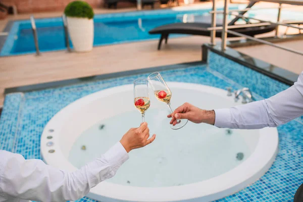 Yaz tatilleri konsept imajı. Güneşli bir yaz öğleden sonrasında, havuz kenarında bir terasta iki bardak soğuk şampanya ve bir tabak çilek. Şerefe.