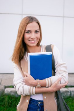 Kitaplar ile ayakta ve kameraya gülümseyen öğrenci