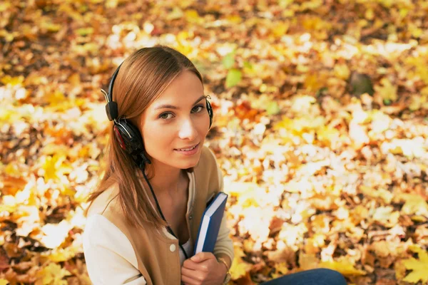 Studentin sitzt mit Kopfhörer zwischen Ahornblättern und schaut nach — Stockfoto