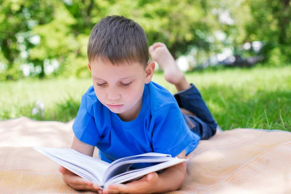 Boy lying on beach mat and reading book — Stock Photo, Image