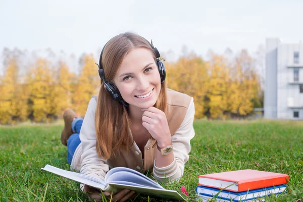 Estudante ouvindo fones de ouvido e segurando livro aberto — Fotografia de Stock