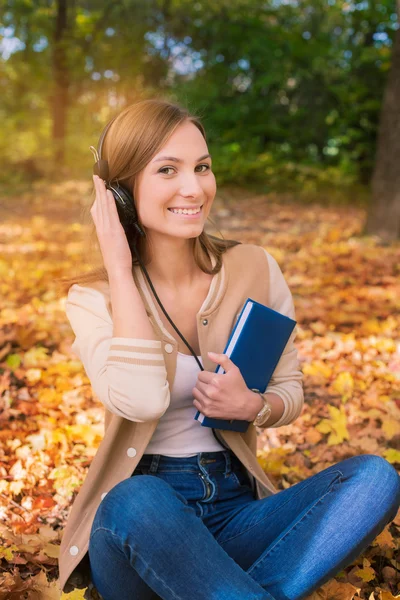 Student sitzt zwischen Ahornblättern, hört Kopfhörer und — Stockfoto