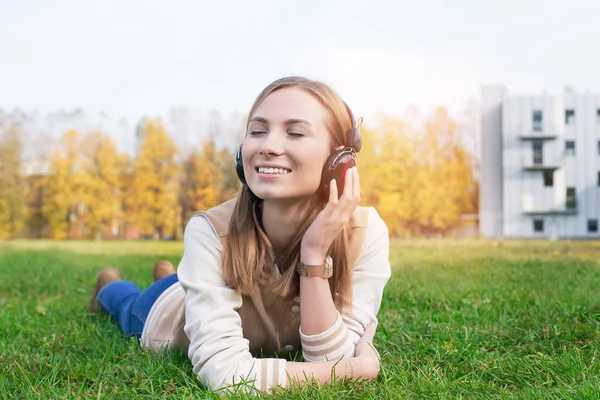 Student liegt im Gras und hört Musik in Kopfhörer — Stockfoto