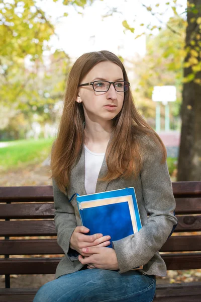 Задумчивый студент в очках сидит на скамейке — стоковое фото