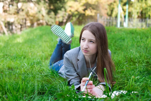 Estudante com fones de ouvido deitado na grama — Fotografia de Stock