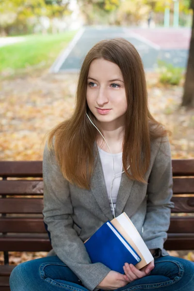 Student sitting on bench with headphones and book — Stok fotoğraf