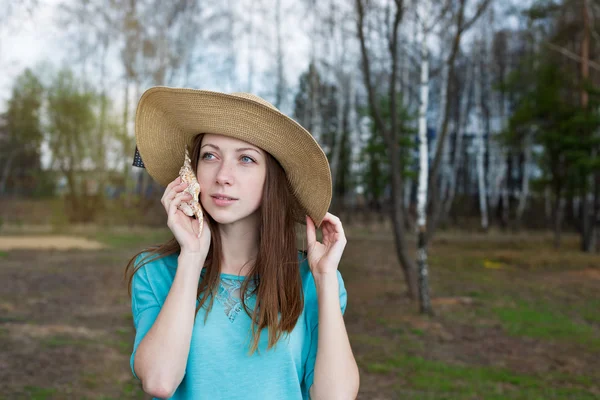 Freckled girl in hat listening to shell — Stock Photo, Image