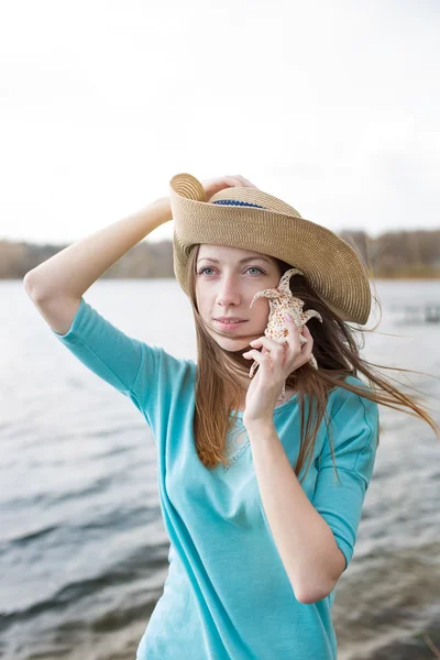 Sommersprossiges Mädchen mit Hut hört Muschel und steht auf dem See — Stockfoto