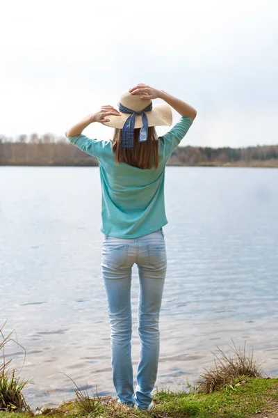 Meisje met hoed reputatie met rug voor meer — Stockfoto