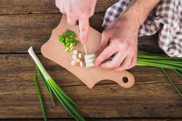 Mann hackt grüne Zwiebel auf dem Brett. Holztisch — Stockfoto