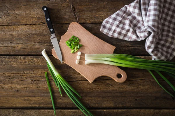 Zöld hagyma, a vágódeszka. Kést, és egy fából készült asztal szalvéta — Stock Fotó