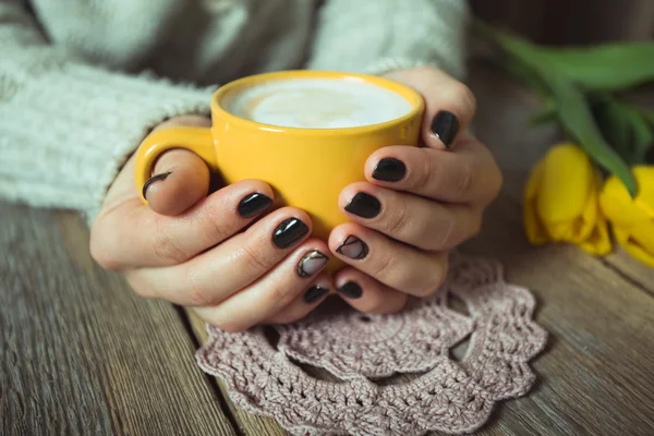 Yellow cup in the hands of women. Gel nail manicures. Phone and the magazine on the table — Stock Photo, Image