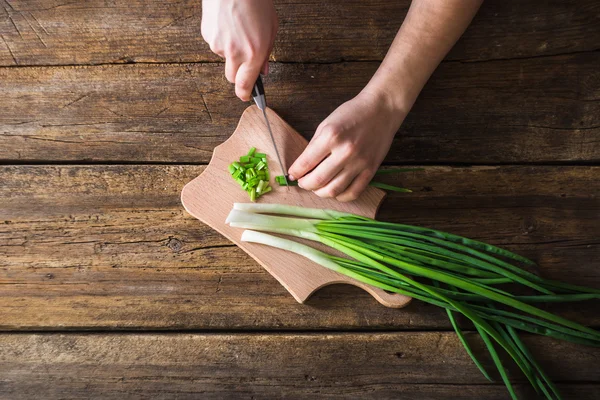 Mann hackt grüne Zwiebel auf dem Brett. Holztisch — Stockfoto