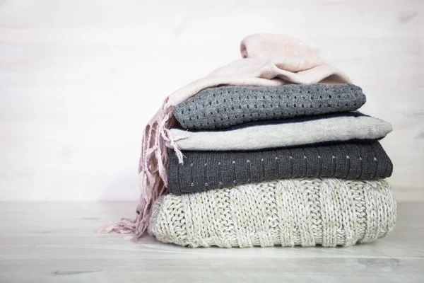 Stack of various woolen sweaters on a white wooden background — Stock Photo, Image